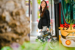 advertising photography of woman stepping off bus with her collapsible bike